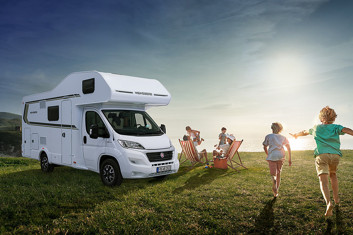 Eine Familie verbringt den Tag draußen auf einer Wiese neben einem Wohnmobil.